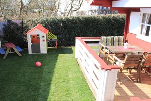 Une terrasse en bois avec une balustrade blanche, une petite maison de jeu et une table avec des chaises.