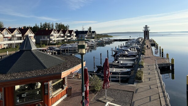 A marina with boats docked, a lighthouse, and residential buildings in the background. - Cozy vacation home in beach location for 4 people and only 100m to the bathing area (Plau am See)