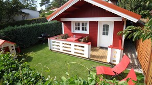 A red and white house with a fenced patio and a small deck. - Cozy vacation home in beach location for 4 people and only 100m to the bathing area (Plau am See)