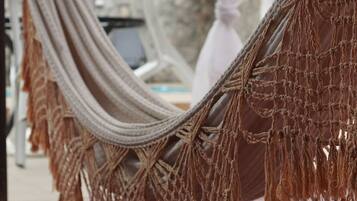 A hammock with macramé hanging from a structure, possibly a balcony or terrace, with a blurred background suggesting an outdoor setting.
