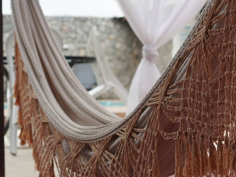 A hammock with macramé hanging from a structure, possibly a balcony or terrace, with a blurred background suggesting an outdoor setting.