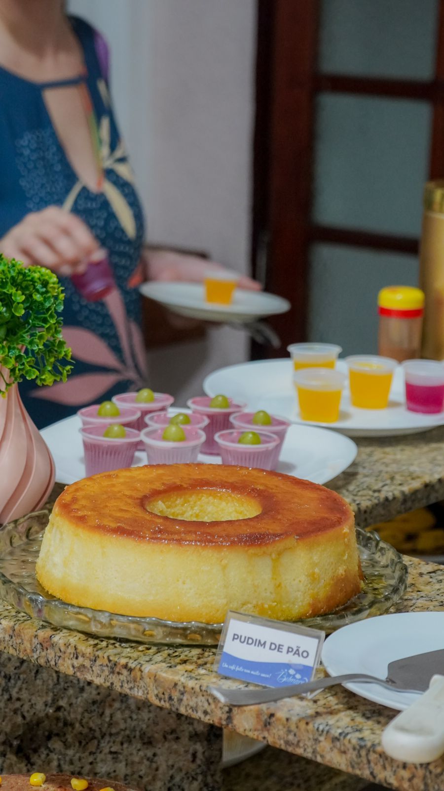 A dessert table with a large cake labeled 'PUDIM DE PÃO' and various small cups with drinks.