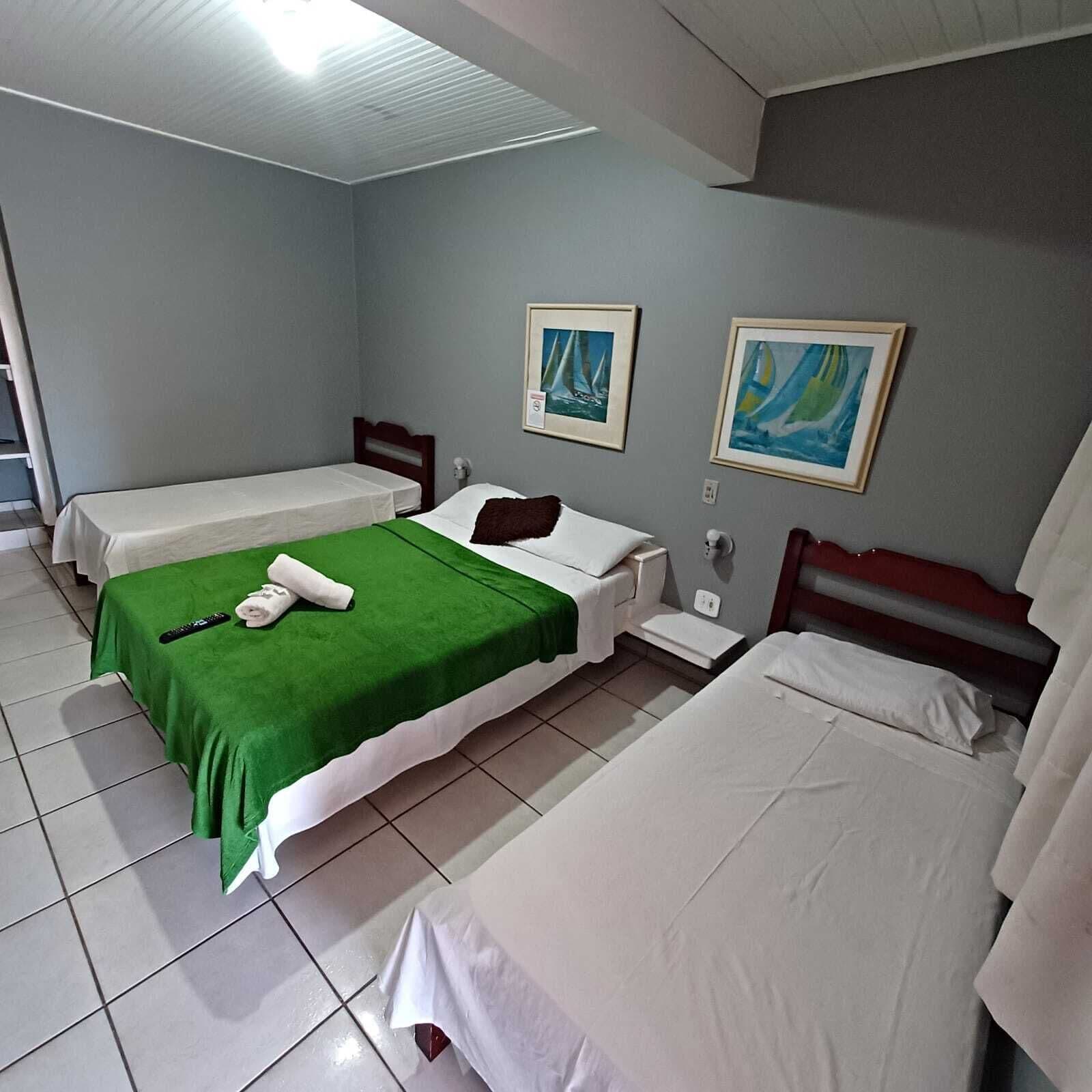 Une chambre d’hôtel avec deux lits simples, une couvre-lit verte sur l’un d’eux et deux tableaux au mur.