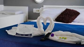 Una habitación de hotel con cama, cubrecama azul, toallas dispuestas en forma de corazón, control remoto, almohada y una nota sobre la cama.