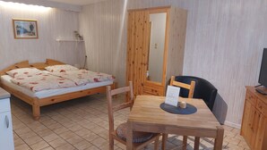 A room with a wooden bed, a wooden table with a chair, a television, and a wardrobe.