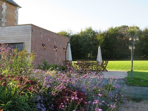 A patio with a brick building, outdoor seating, and a garden with flowers.