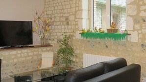 A living room with a stone wall, a flat-screen TV, a glass coffee table, a black leather sofa, and a window with a view of a building.