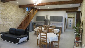 A spacious living area with a stone wall, wooden staircase, and a kitchen in the background.