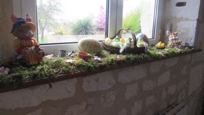 A window sill with a mossy ledge, a ceramic bear figurine, a basket with eggs, and a small bird figurine.
