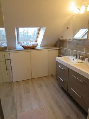 A modern bathroom with a skylight, a large mirror, and a wooden floor.