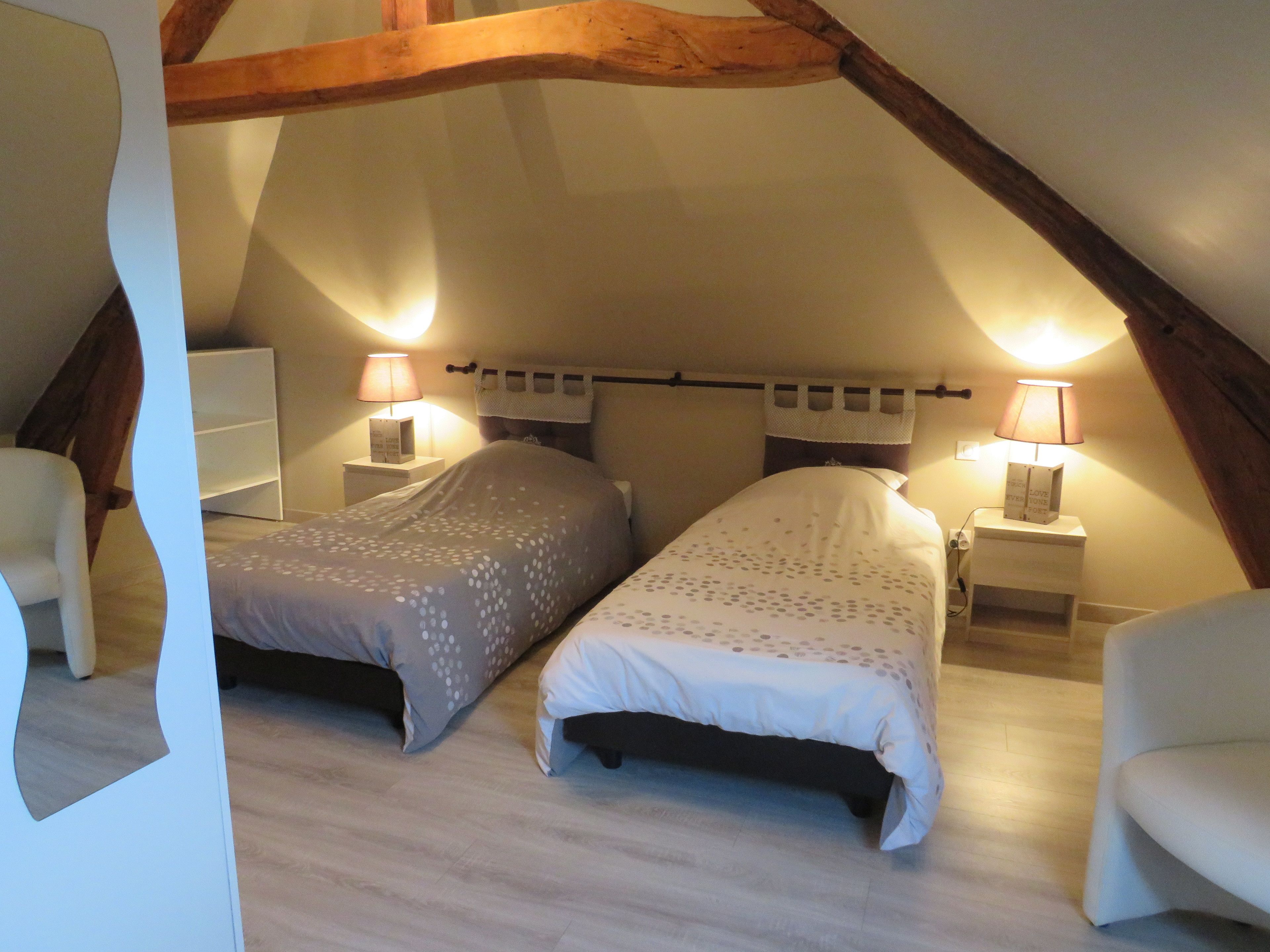 Un dormitorio con dos camas, vigas de madera, lámparas de noche y un aparador blanco.