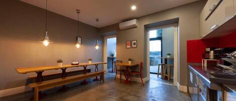 A modern kitchen with a red accent wall, a dining area with benches, pendant lighting, and an open layout leading to a balcony.