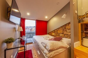 A modern bedroom with a stone accent wall, a bed with white linens, a red curtain, and a city view. - The Bridge (Lisbon)