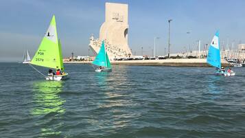 A coastal scene with sailboats on the water, a prominent monument in the background, and a clear sky.