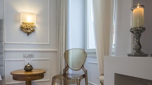 Une pièce avec un plancher en bois, une table ronde avec une lampe, une chaise et une console blanche sur laquelle est posée une bougie.