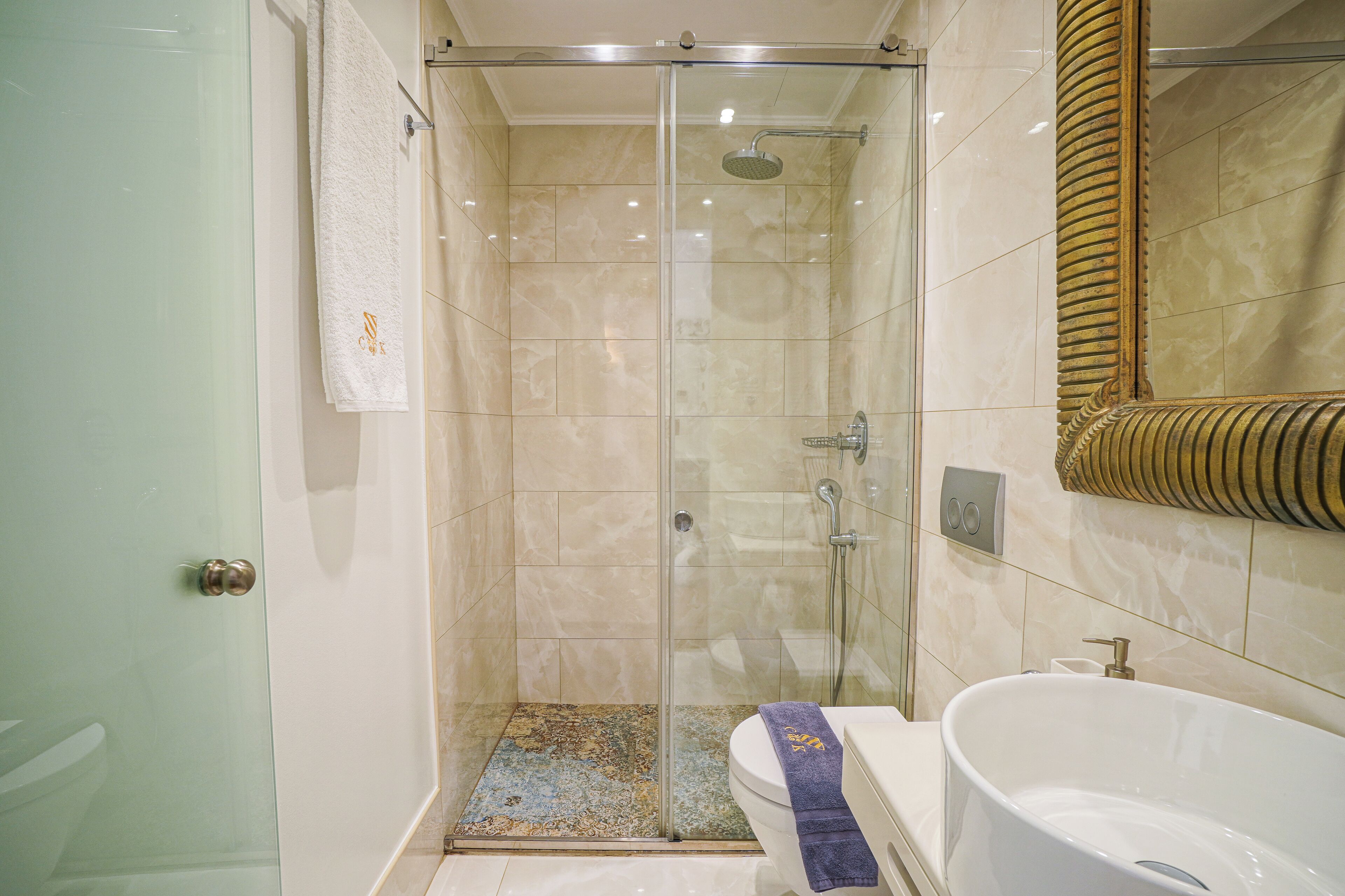 A glass-enclosed shower stall with a showerhead, a toilet with a towel, and a bathtub with a faucet.