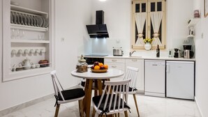 Une cuisine moderne avec des meubles blancs, une table de salle à manger ronde accompagnée de deux chaises, un four encastré et une machine à café.