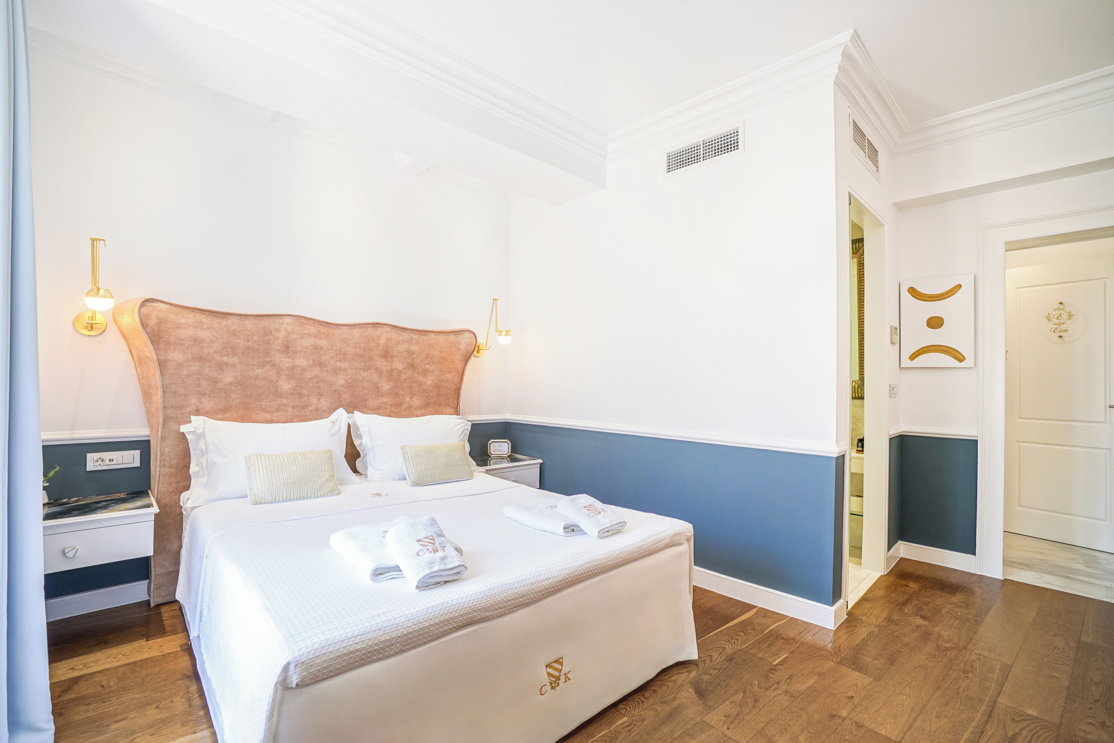 A neatly made bed with white linens and towels, a wooden nightstand with a lamp, and a blue accent wall.