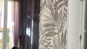 Un comedor con una mesa de madera, sillas negras, una cortina y una pared con diseño de hojas.