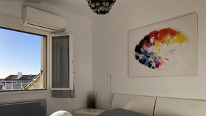 Un dormitorio con cama, ventana con vistas, radiador, mesita de noche y una obra de arte en la pared.