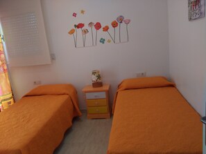 A room with two beds, a small wooden nightstand, and a wall decoration of flowers.