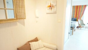 Une petite pièce, bien rangée, avec un lit, une lampe fixée au mur et une fenêtre équipée de stores.