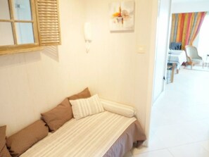 A small, neatly arranged room with a bed, a wall-mounted light, and a window with blinds.