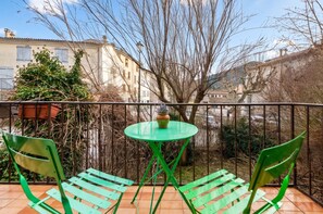 A balcony with a green table and chairs, overlooking a cityscape with buildings and trees. - Homerez - Apartment in Barrême (Barrême)