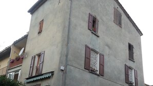 Un immeuble de deux étages doté d’un balcon, avec un vélo garé devant et un petit portail à l’entrée.
