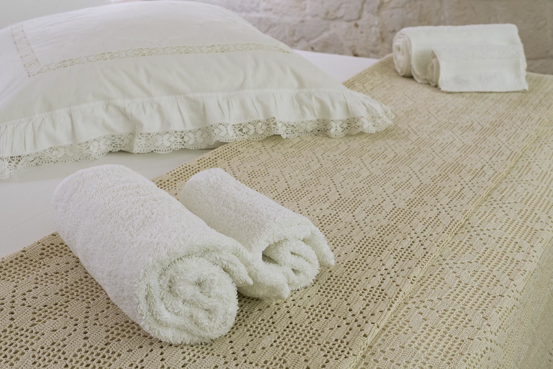 A neatly made bed with a white pillow and two rolled white towels.