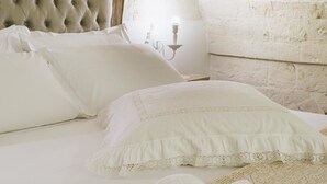 A bed with white linens and lace details, a wooden headboard, and a white wall with a textured finish. - B&B C'era una volta (Alberobello)