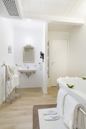 A modern bathroom with a white sink, mirror, and bathtub. There is a towel rack with a towel and a pair of slippers on a mat.