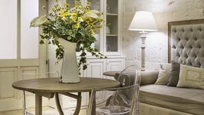 A room with a round wooden table, a white vase with flowers, a clear chair, a cushioned sofa, and a lamp. - B&B C'era una volta (Alberobello)