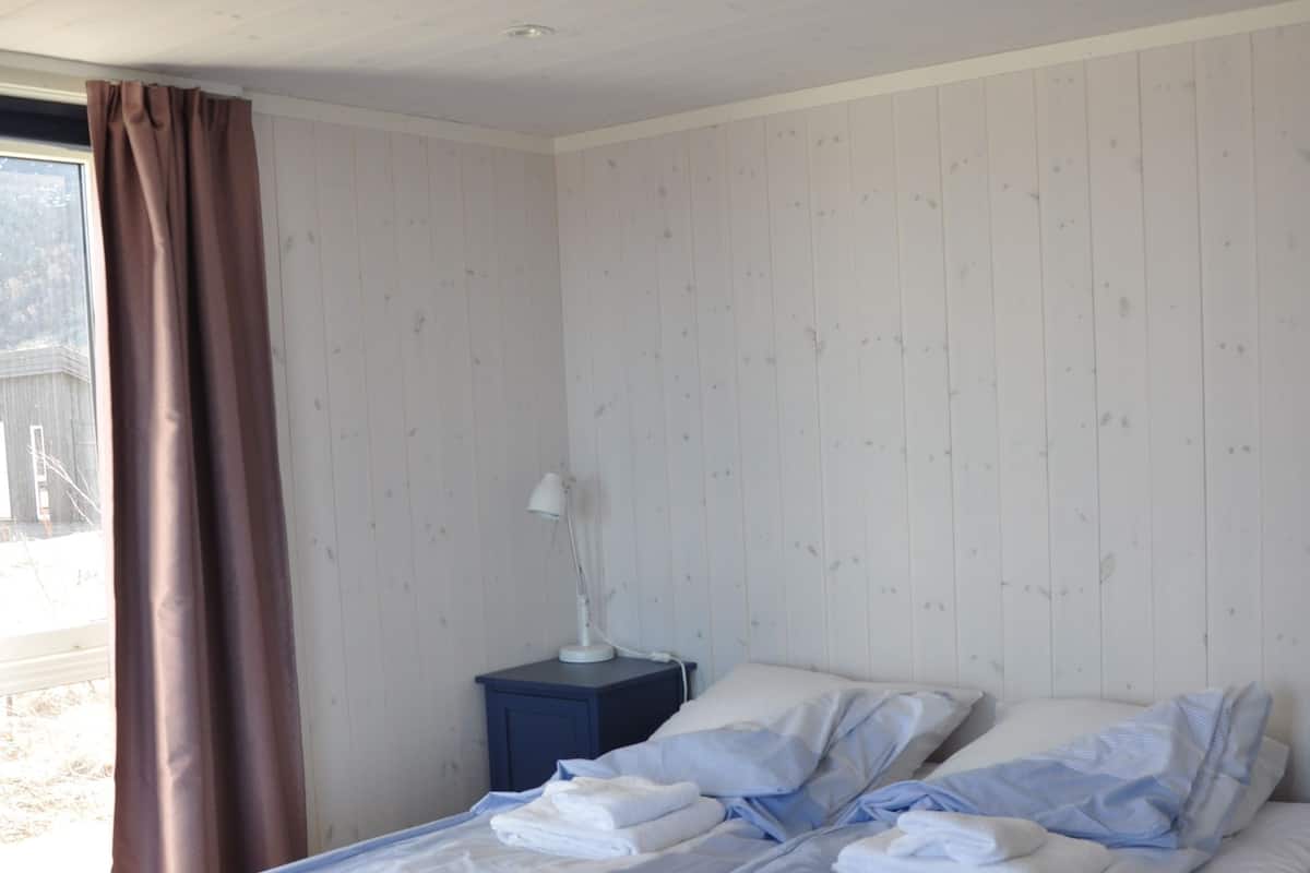 A bedroom with a bed, a nightstand, a lamp, and a window with curtains.
