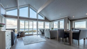 Una habitación amplia con ventanas grandes, techo de madera y un comedor con sillas y mesa.