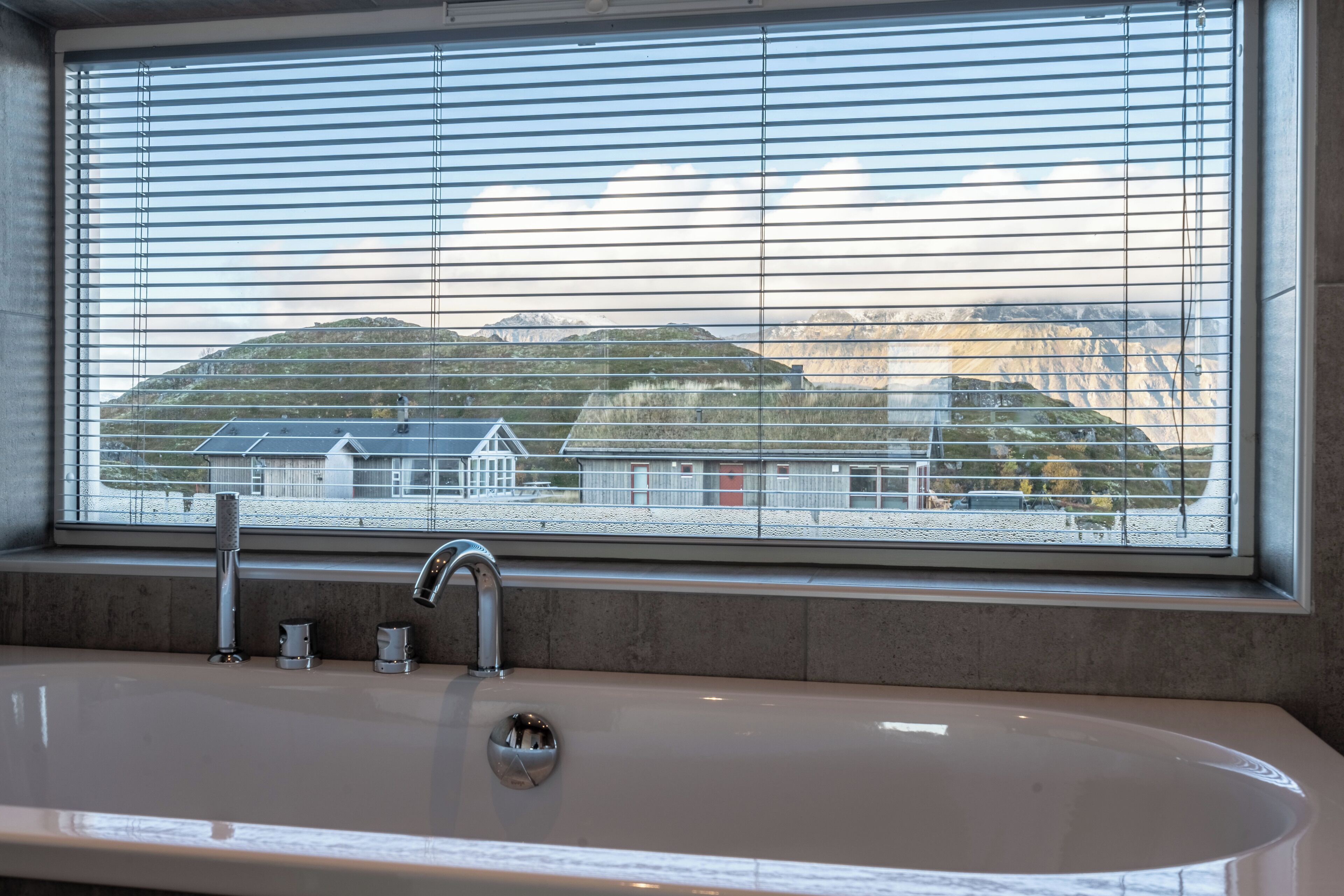 A bathroom with a bathtub, a faucet, and a window with blinds.