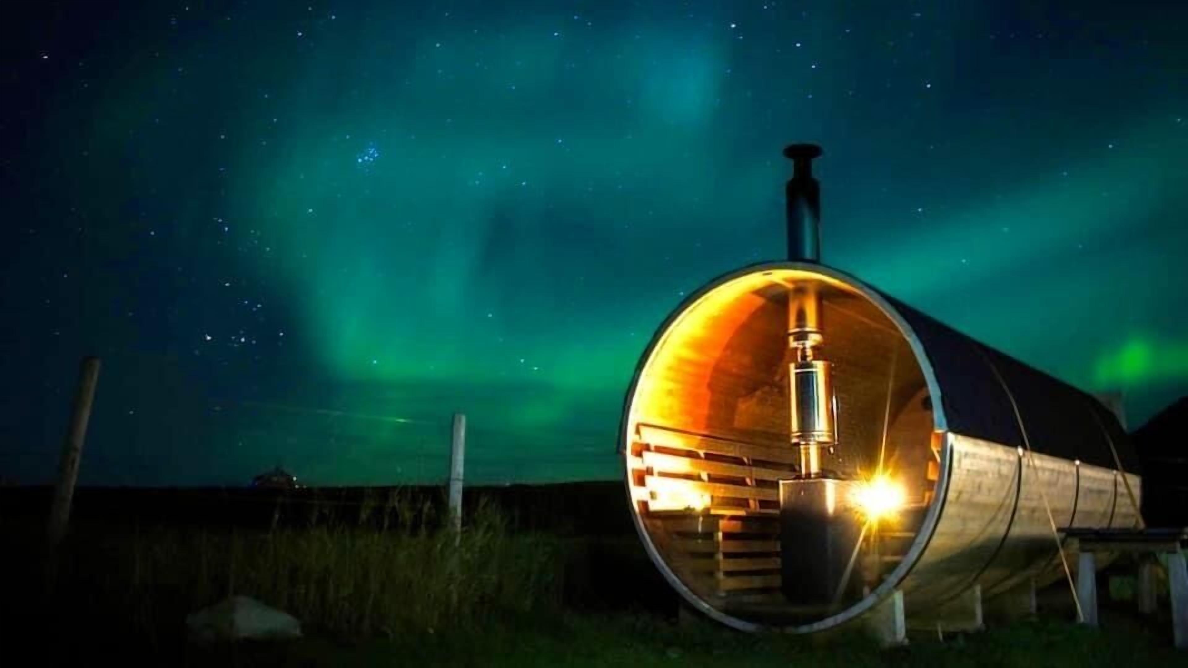 A cylindrical building with a visible interior, illuminated by warm light, set against a night sky with visible stars and the aurora borealis.