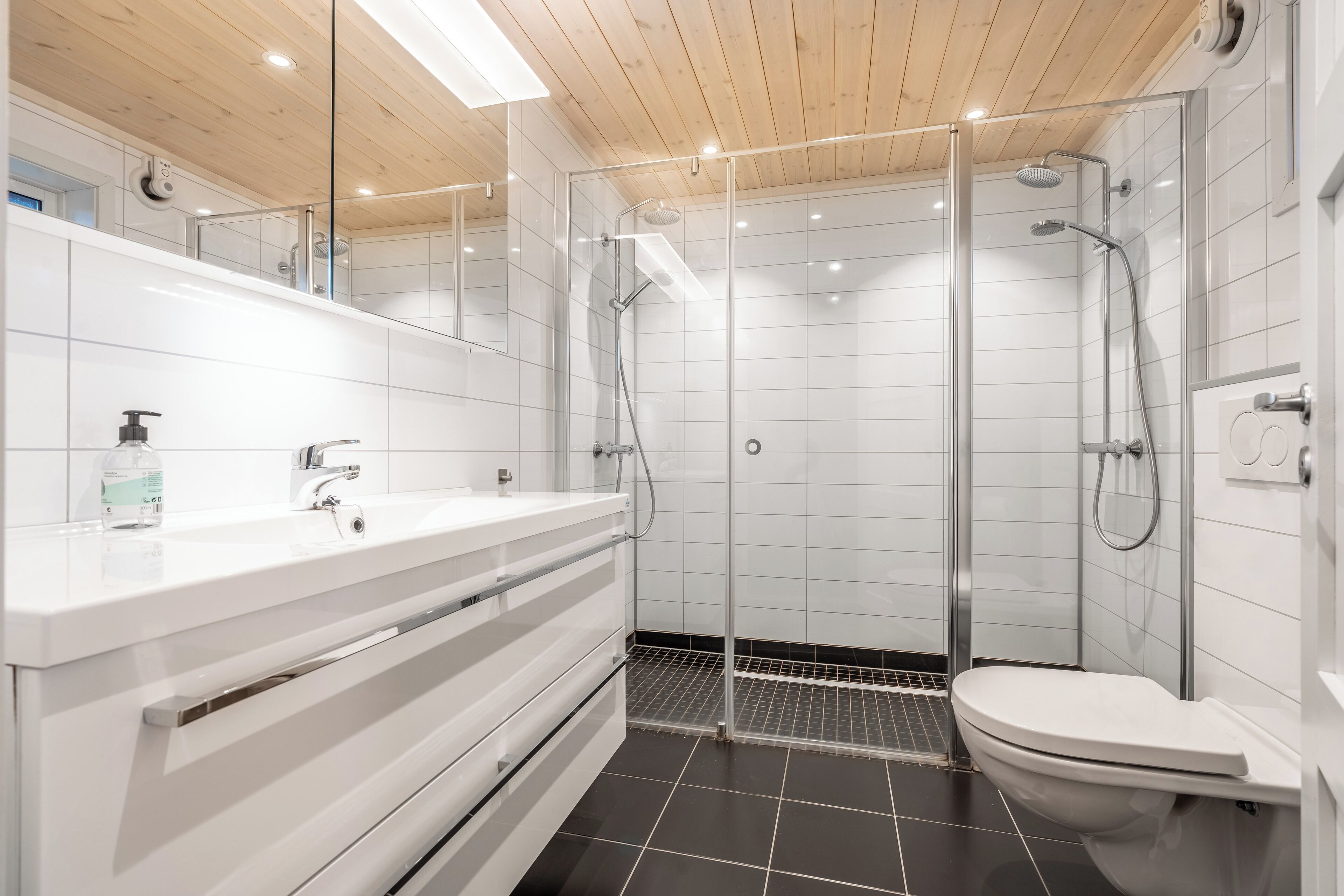 A modern bathroom with a glass-enclosed shower, white tiles, and a wooden ceiling.