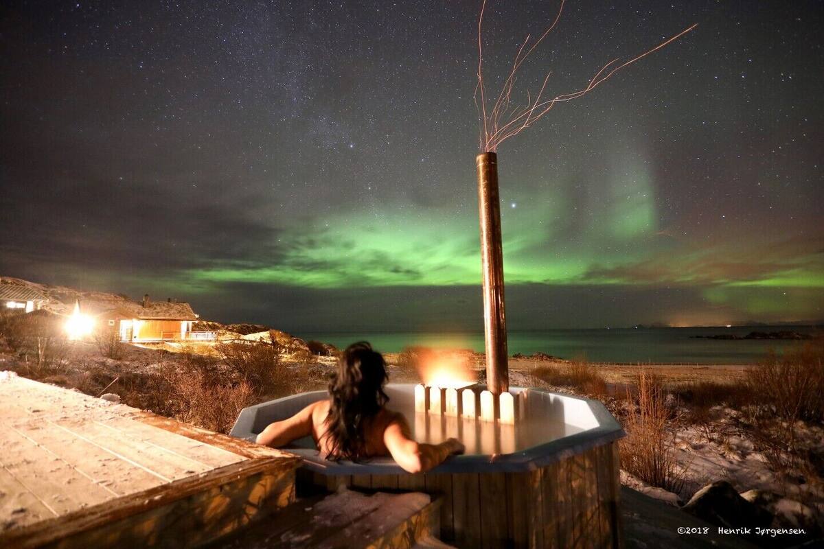 A person relaxing in a hot tub with a view of the Northern Lights.