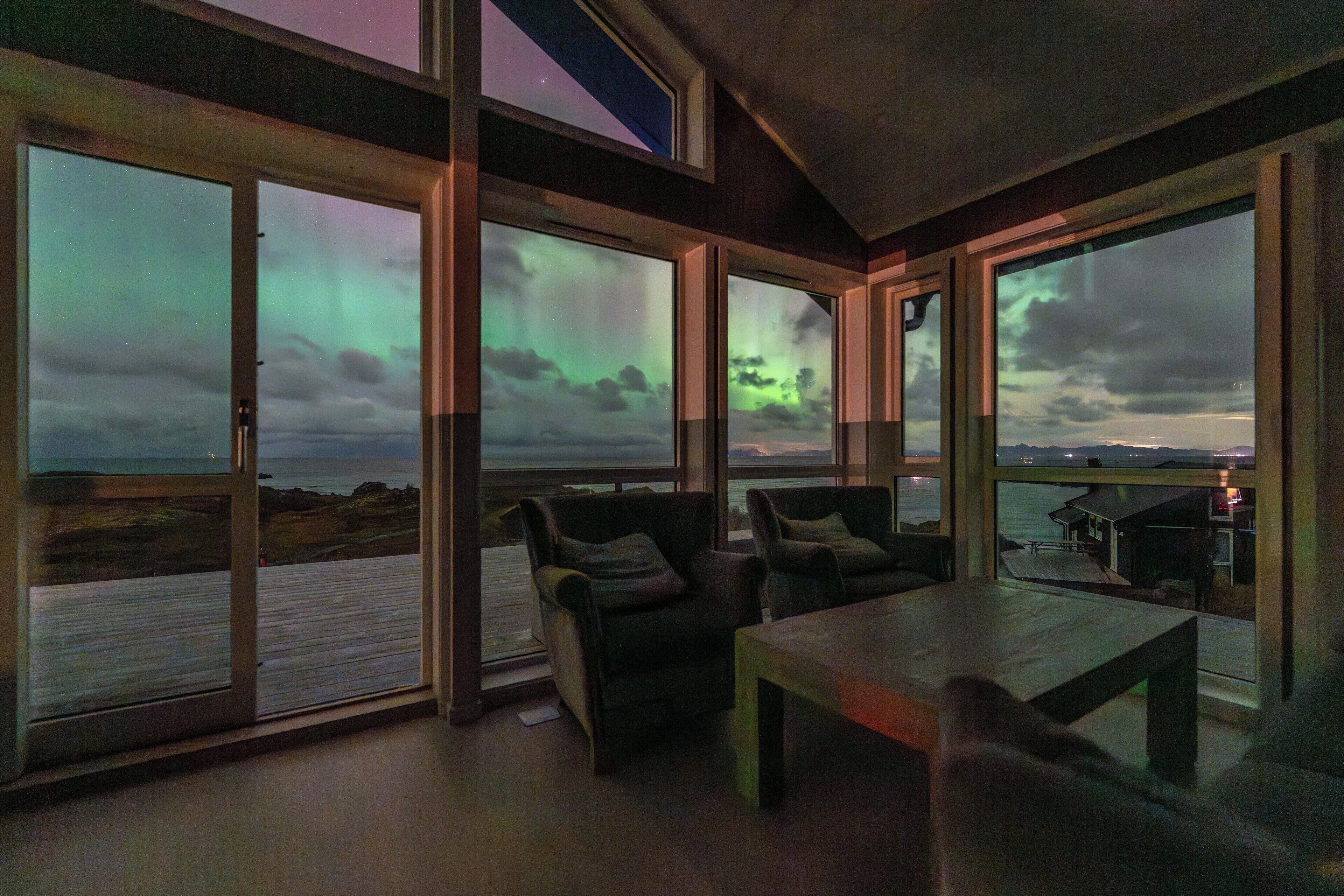 Un interior moderno con amplios ventanales que dan a una terraza, mostrando vistas del océano y un cielo nublado.