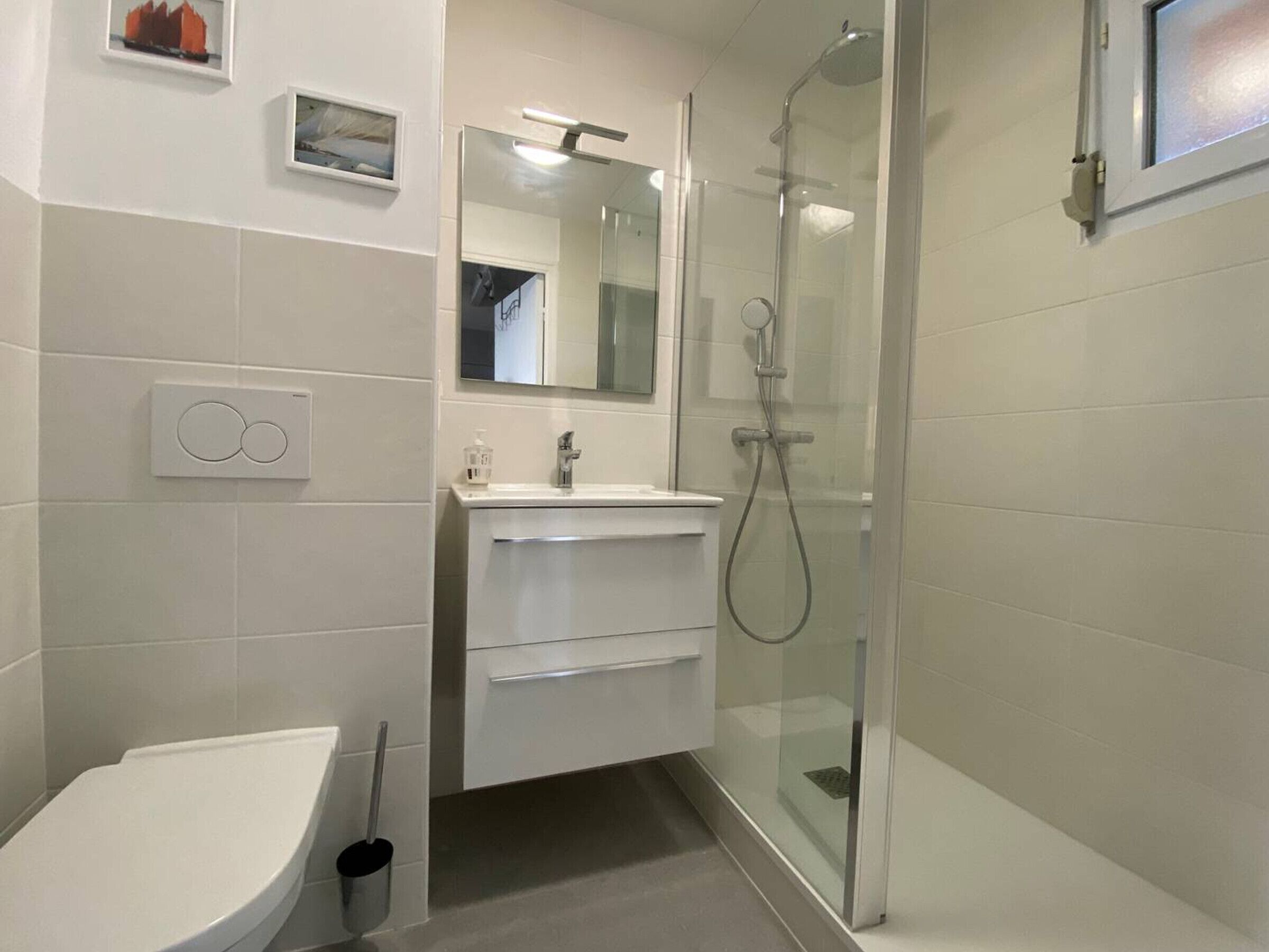 Un baño moderno con inodoro, lavamanos y ducha con cerramiento de vidrio.