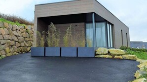 A modern building with a flat roof, large windows, and a stone wall on one side. - Modern Single-Level House with WiFi, Terrace, and Parking in Trégastel (Trégastel)