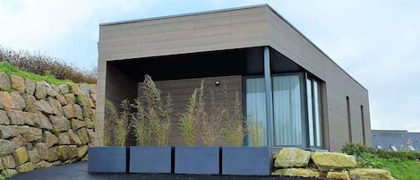 A modern building with a flat roof, large windows, and a stone wall on one side.