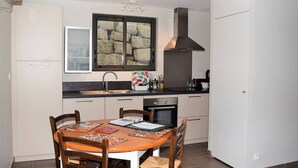 A compact kitchen with a dining area, featuring a built-in oven, a large window with a stone backsplash, and a modern stove. - Modern Single-Level House with WiFi, Terrace, and Parking in Trégastel (Trégastel)