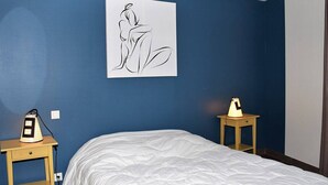 A bedroom with a blue wall, a white bed, and a black and white abstract painting. There are two bedside tables with lamps. - Modern Single-Level House with WiFi, Terrace, and Parking in Trégastel (Trégastel)