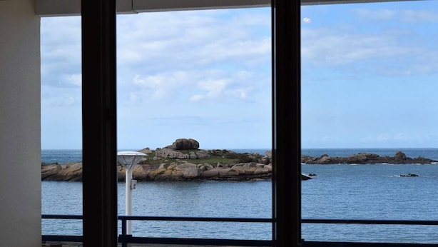 A balcony with a view of the sea, featuring a table and chairs, and a rocky coastline in the background. - Apartment with WIFI, Beachfront, Private Parking, Pets Allowed (Trégastel)