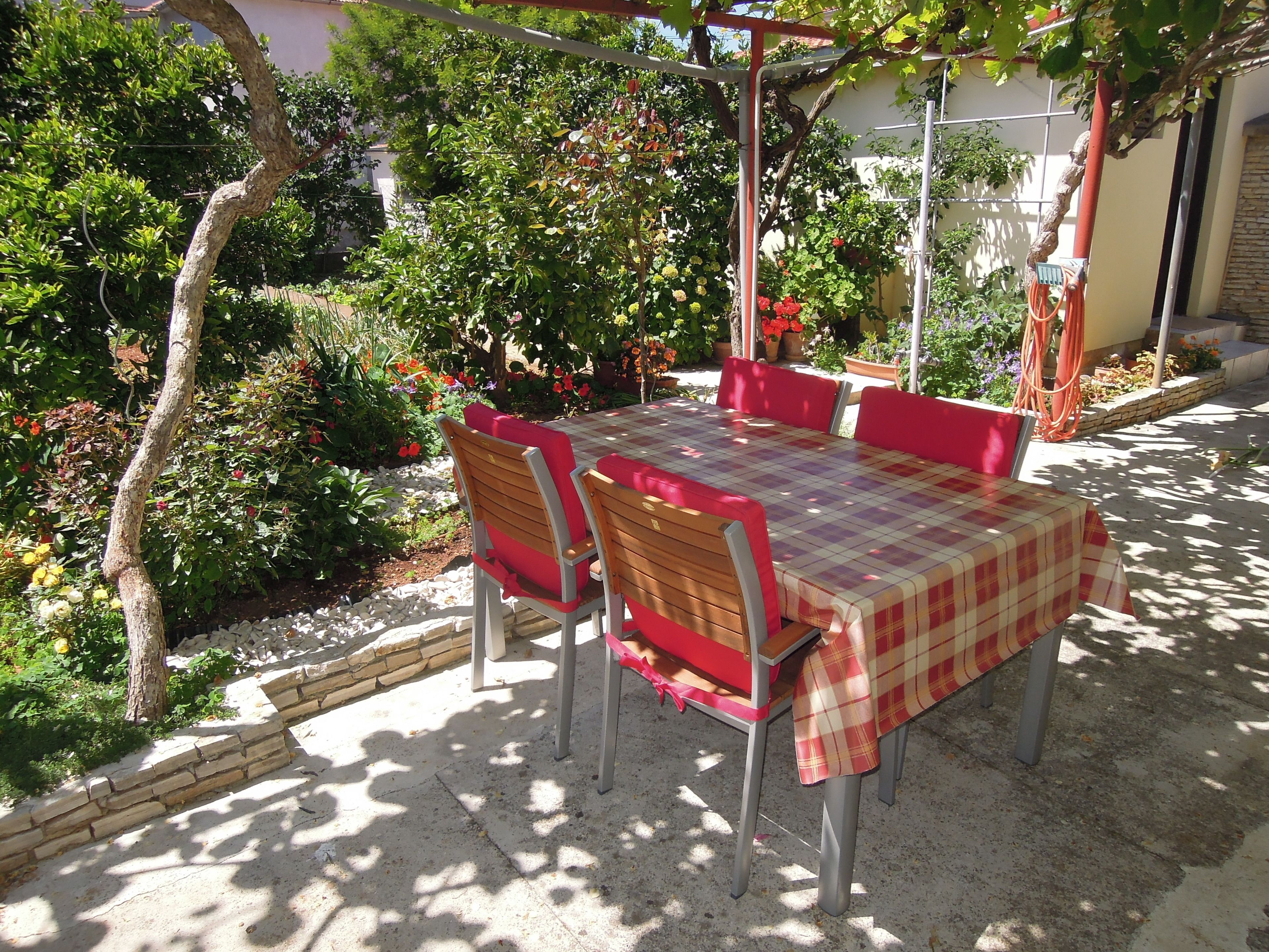 An outdoor patio with a table and chairs, surrounded by lush greenery and flowering plants.