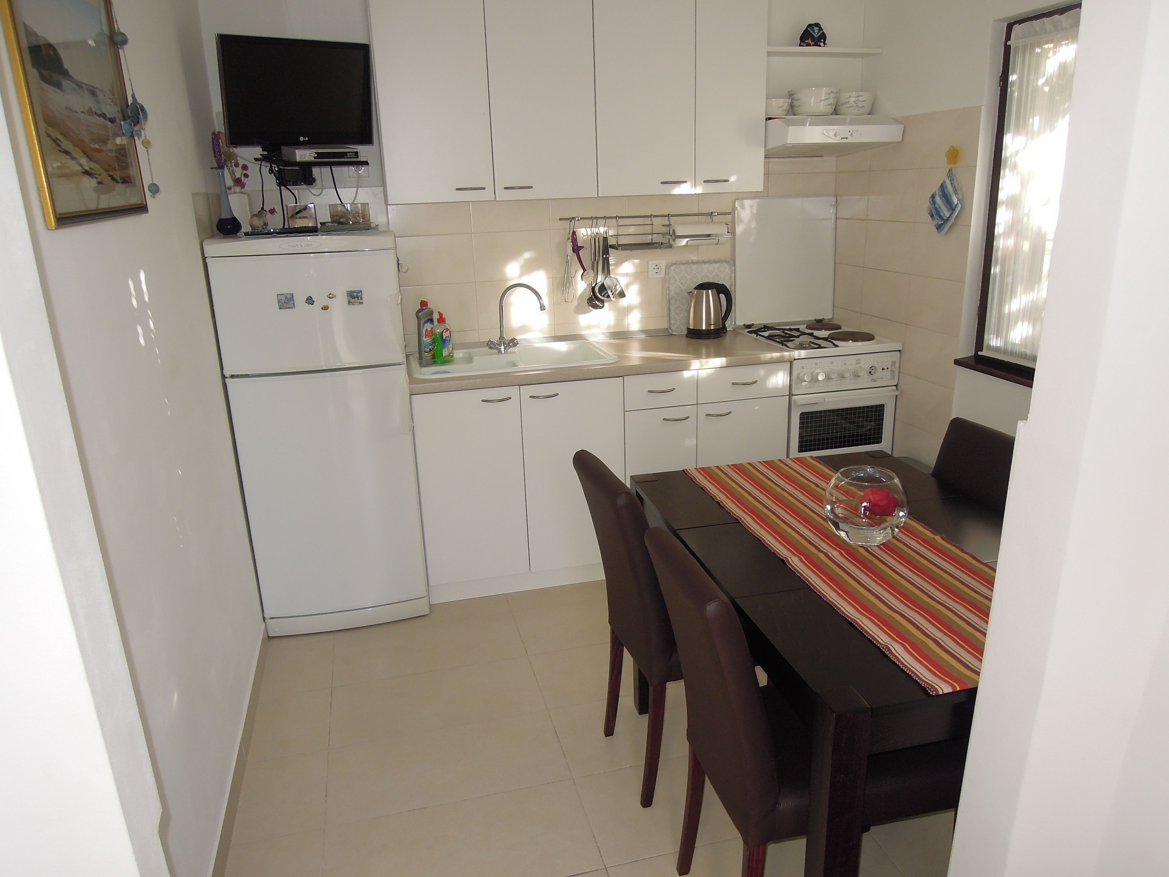 A compact kitchen with white cabinets, a dining table with chairs, a TV, and a stove.