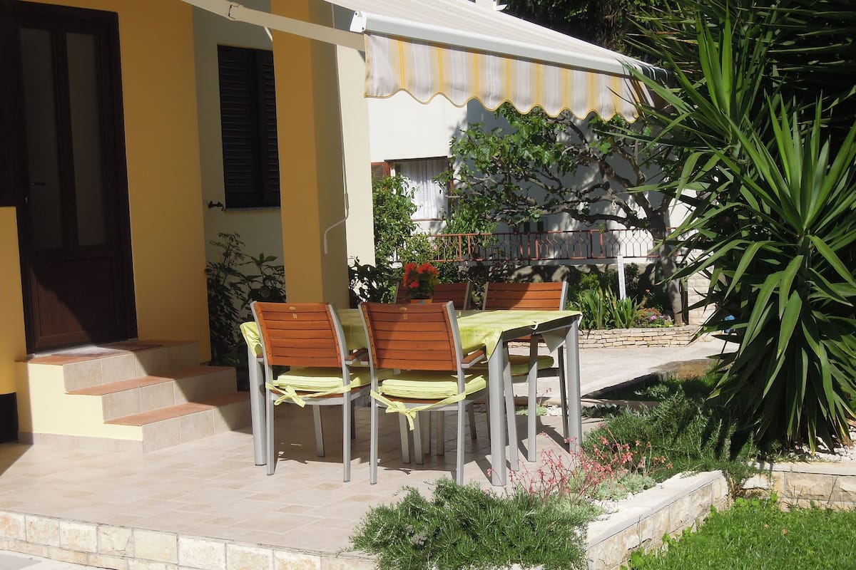 A patio with a table and chairs, a yellow wall, and a white awning.
