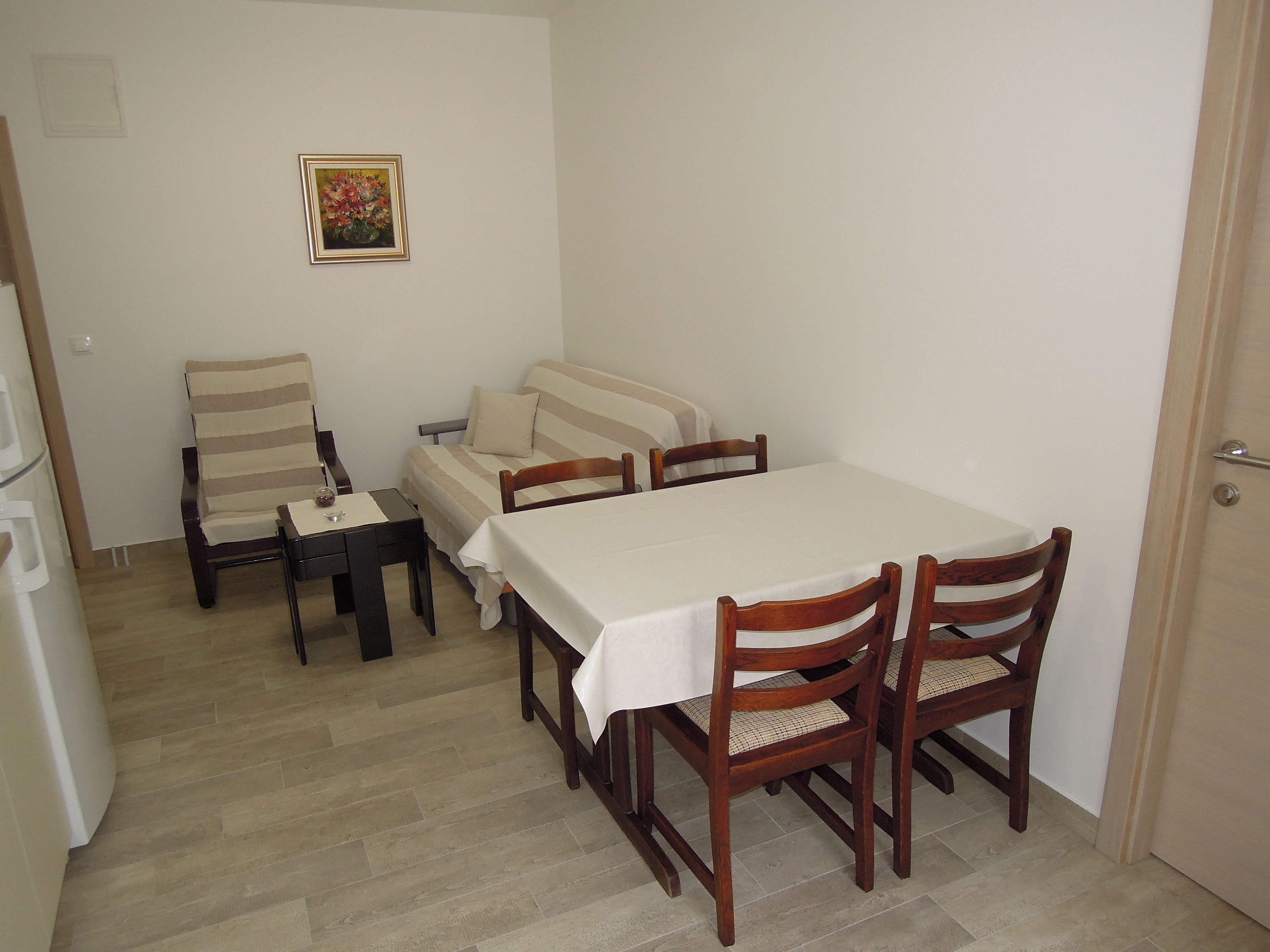 A dining area with a table and chairs, a sofa, and a small table with a glass and a bottle.
